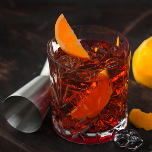Glass of non-alcoholic negroni with a shot measure and garnished with an orange