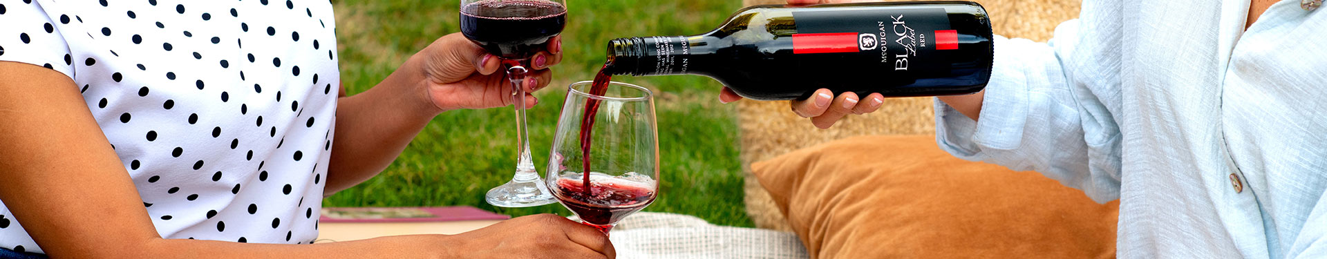 Two women enjoying a bottle of Black Label Red in a picnic setting.