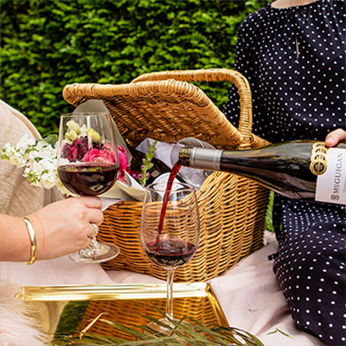 Woman wearing a navy and white polka dot dress pouring a glass of McGuigan red wine at a picnic