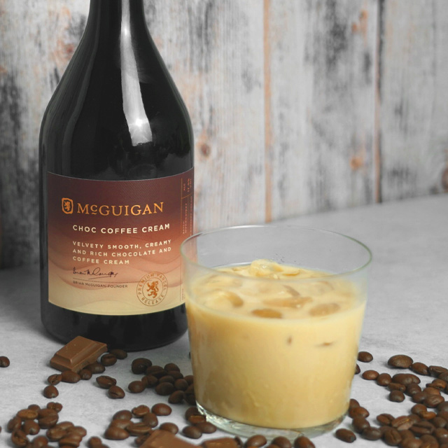 Bottle of McGuigan choco coffee cream next to a glass of McGuigan choco coffee cream over ice with coffee beans