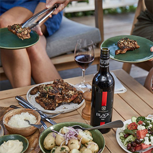 bottle of McGuigan Black Label Red with BBQ lamb being served to various individuals