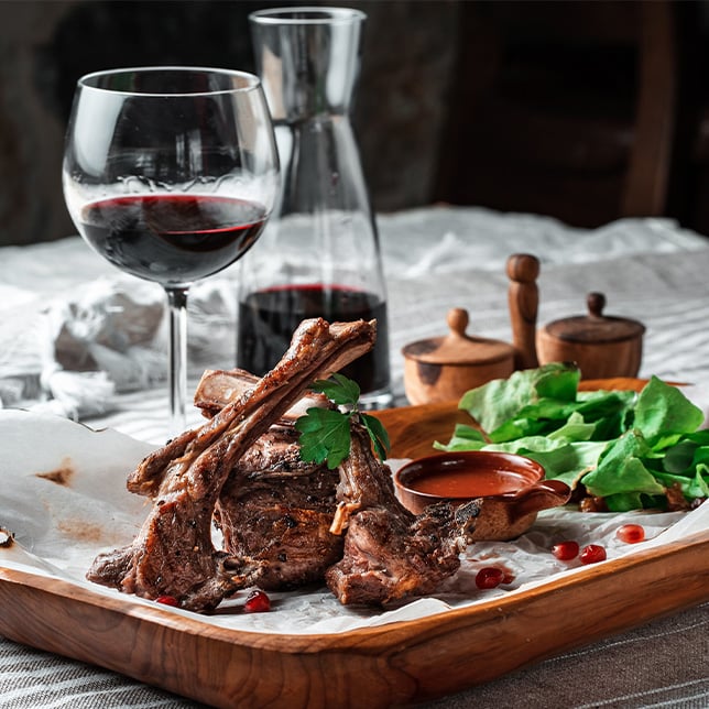 beef with a glass or red one on a plate with wine in a bottle at the back and sauce next to the meat