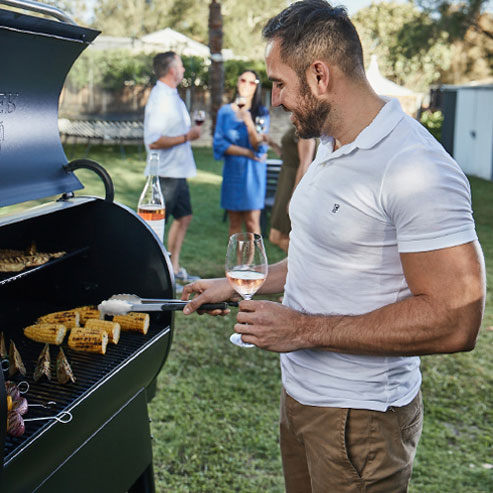 Man holding a glass of rose whilst using a BBQ