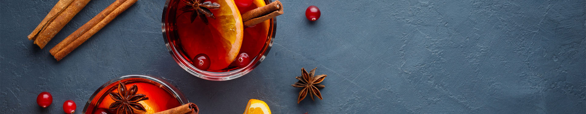 Two glasses of mulled wine surrounded by spices and oranges