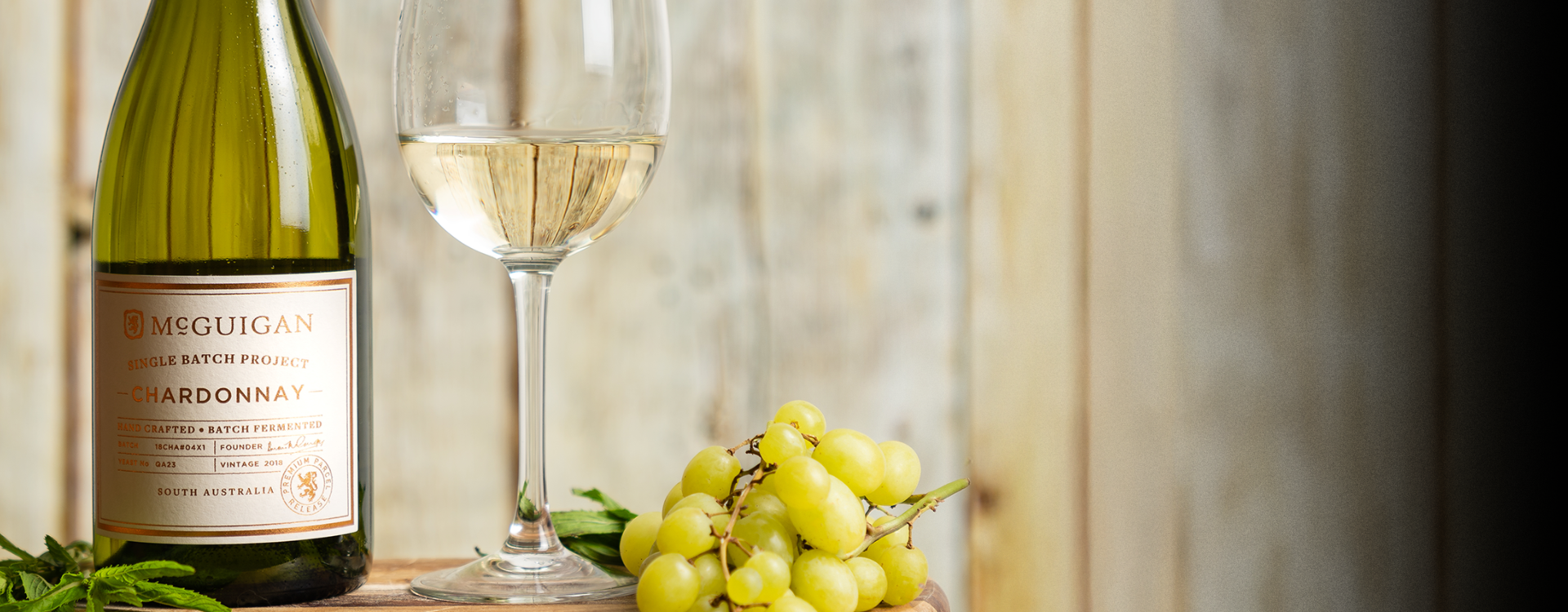 McGuigan Single Batch Chardonnay with wooden textured background alongside a bunch of green grapes.