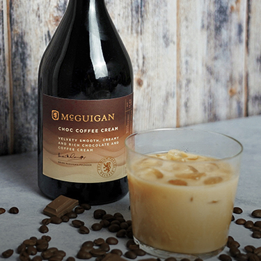 Glass and Bottle of McGuigan Choco Cream with coffee beans, against a grey background