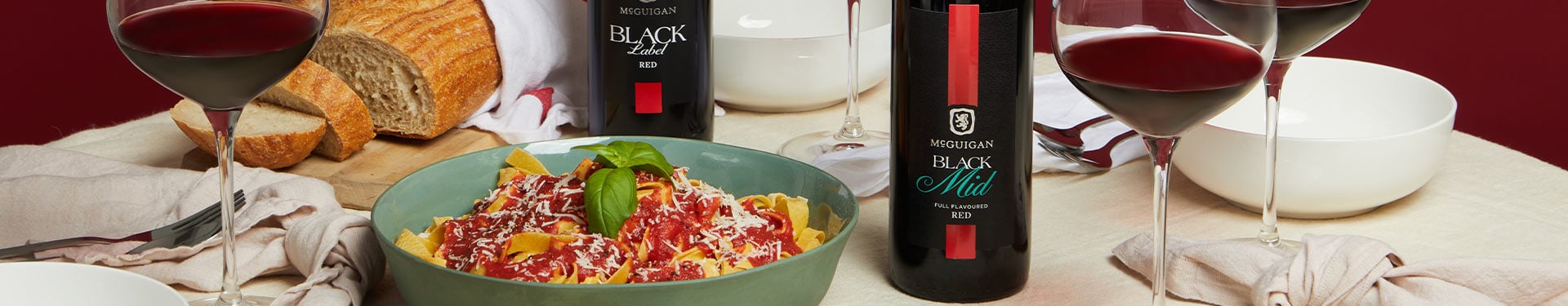 A bottle of McGuigan Black Label Red and Black Label Red Mid in a dinner table setting.