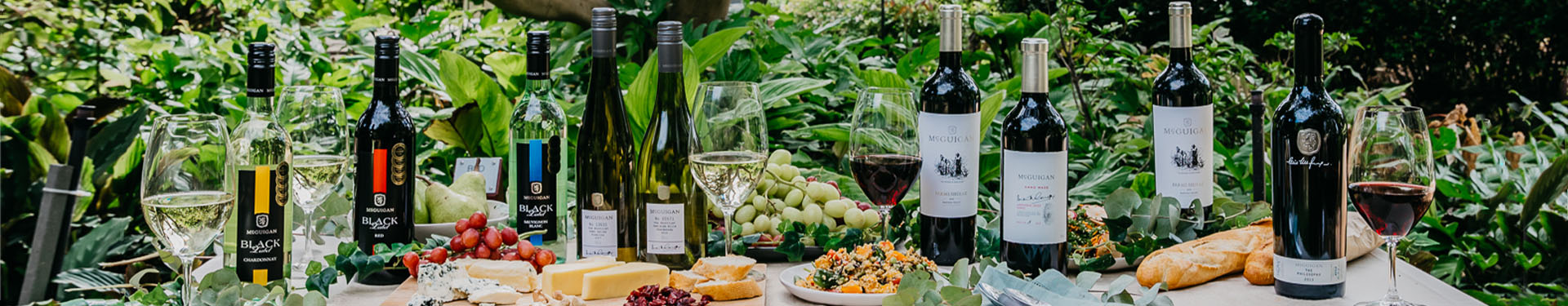 Various McGuigan wine varietals outdoors on a table with grapes, bread and cheese