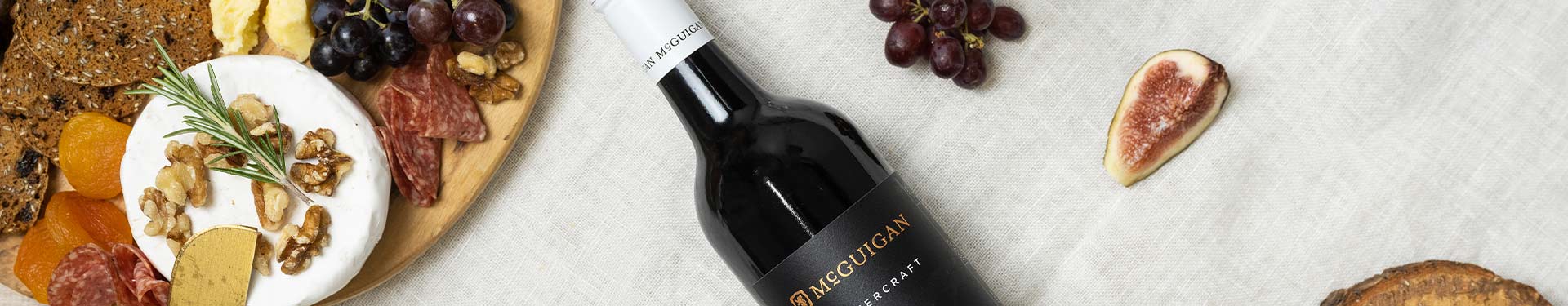 Bottle of McGuigan Noon Harvest Merlot lying on a table with a cheeseboard