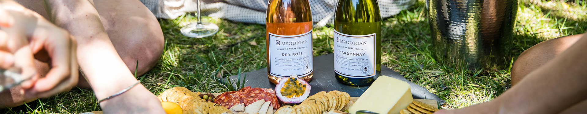 Two glasses and a bottle of McGuigan rose outdoors in a picnic setting