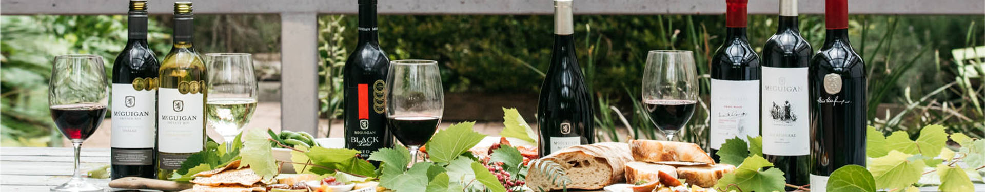 Various different bottles of McGuigan wines outdoors with a charcuterie board containing cheeses and crackers